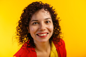 Studio shot of positive and the smiling pretty female. Curly girl in bright red shirt and yellow t-shirt. Isolated on yellow background. Close up.