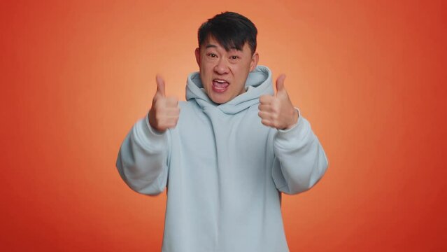 Nice, good job. Asian handsome businessman man showing thumbs up and nodding in approval, enjoy successful great work. Adult guy isolated alone on orange studio background. People lifestyle concept