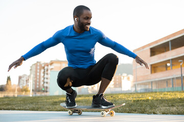 A dark-skinned man has fun riding a skateboard in an outdoor park, the guy sits while sliding down...