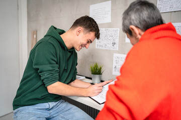 Fototapeta premium One student teenage caucasian man study learn with help of his tutor professor or mother senior woman at home having private lesson to prepare for exam education concept real people copy space