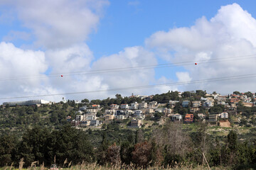 Cute town on a hill. Colorful buildings of Israel's village. Green grass, blue sky with fluffy clouds. Architecture of Israel. Spring in Middle East. 