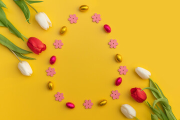 Flat-lay Easter decoration wooden flowers, rabbits and eggs,tulips on yellow background. Copy space.