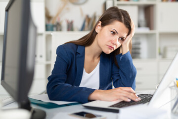 Portrait of frustrated female entrepreneur sitting at office desk with papers and laptop