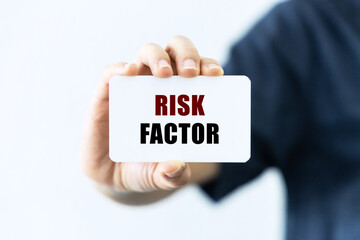 Risk factor text on blank business card being held by a woman's hand with blurred background. Business concept about risk factor.