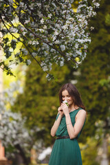 Fototapeta premium Woman-spring. Young woman in long green dress in a blooming apple garden. Spring story. Brown-haired girl with long hairs. 
