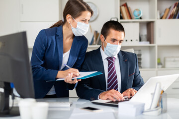 Director in protective medical mask gives instructions to secretary in office