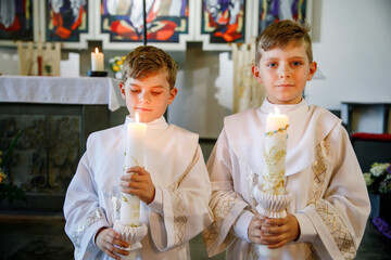 Two little kids boys receiving his first holy communion. Happy children holding Christening candle....