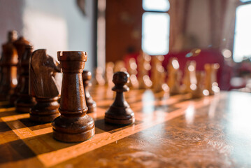 Closeup of wooden brown chess pieces arranged on chessboard over wooden table in alpine hotel room