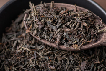 Dry leaves of black tea on brown wooden spoon. Natural Herbal tea, close up.
