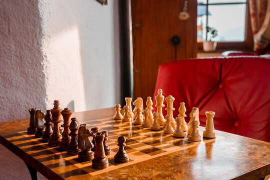 Closeup of wooden brown and white chess pieces arranged on chessboard over wooden table in luxury hotel room