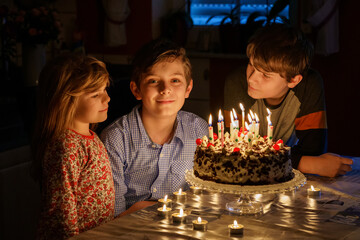 Happy preteen boy celebrating birthday. Preschool sister child and two kids boys brothers blowing...