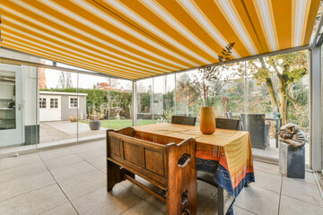 an outdoor dining area with a table and chairs under a yellow striped awning over the outside patio, looking out to the backyard - obrazy, fototapety, plakaty
