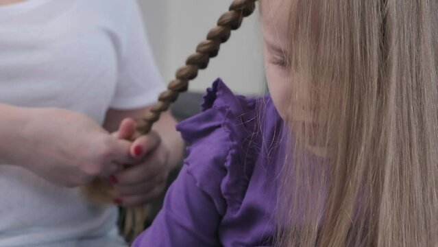 Young loving mother brushing kid daughters hair and styling hairdo braid hairstyle at home getting ready for scool or going out