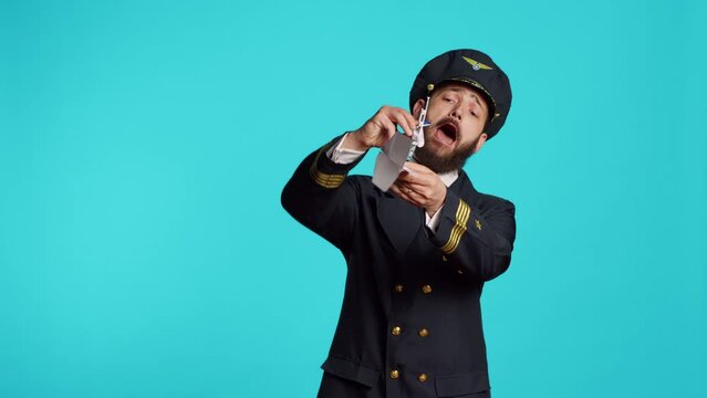 Aircrew captain playing with paper and toy airplane, having fun with origami and small artificial plane on camera. Professional aviator wearing airline uniform working on commercial flights.