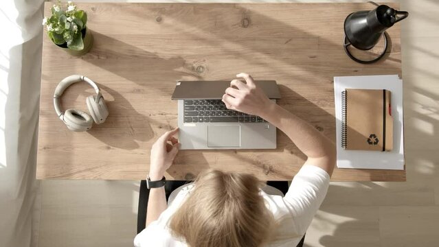 Top down view of unrecognizable woman at work desk, open laptop and start working in office or home office with sunlight from window. Freelancer early morning at home.