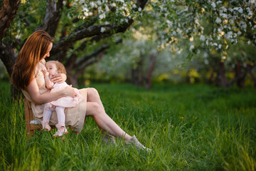 Toddler girl on mom's arms in apple garden. breast feeding in blooming apple garden. Mom loves her child. Spring story. Happy family at spring day. Mother and little daughter tenderness relations
