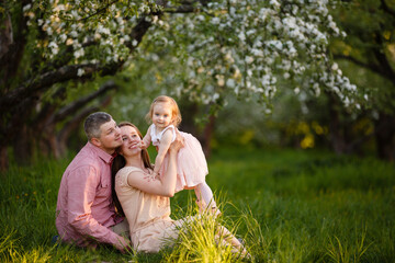 little daughter with parents on a picnic in blooming apple garden. Mom loves her child. Spring story. Toddler girl with family in apple garden. Happy family in beautiful spring day. Tender relations