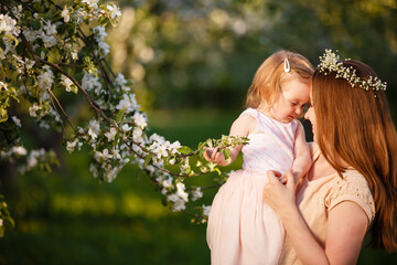 Mother and little daughter play in blooming apple garden. Mom loves her child. Spring story. Toddler girl in apple garden. Happy family in beautiful spring day