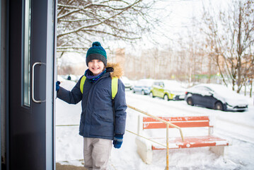 a boy opens the door to the entrance in winter, the child returns from school in cold weather alone