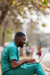 African Man with laptop computer outdoors , doing remote banking and financial transactions online.