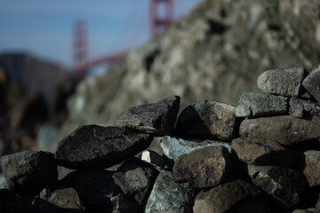 A stack of rocks form a wall at the beach, expressing order and tranquility in nature. In the distance, the Golden Gate Bridge is visible.