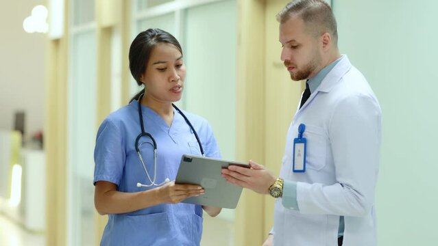 Doctor And Nurse Working In Hospital, Caucasian Male Doctor And Asian Female Nurse Discussing Work In Hospital Female Nurse And Male Doctor Looking At Data On Tablet