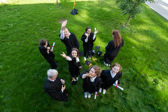 Classmates In Graduation Gowns Throw Their Caps. View From Above. 