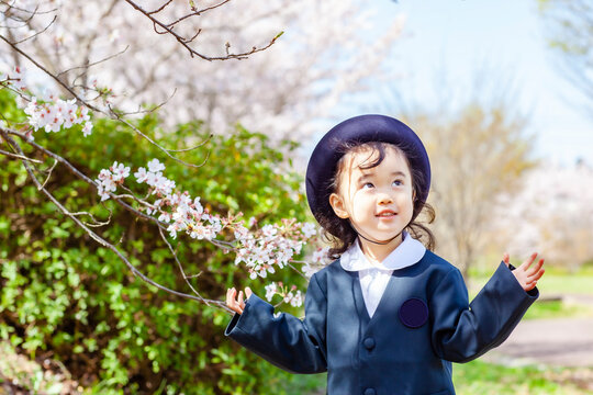 桜の側で幼稚園の制服を着た3歳の女の子
