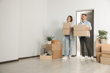 Happy couple with moving boxes entering in new apartment