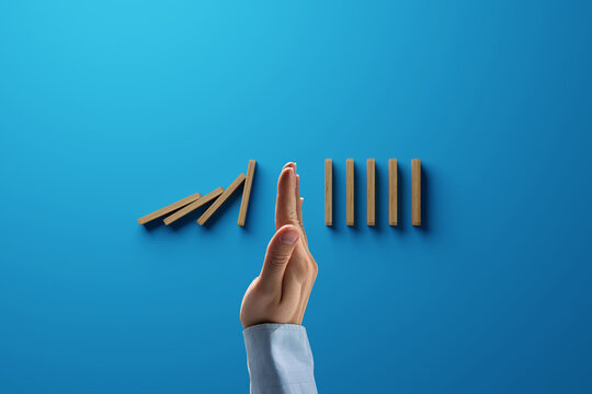 Dominoes falling over, stopped by hand. The concept of insurance, safety for people and personal goods, collapse protection.