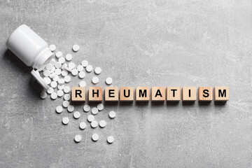 Word Rheumatism made of cubes and pills on light gray textured background, flat lay