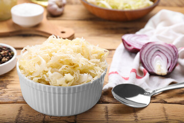 Bowl of tasty sauerkraut and ingredients on wooden table, closeup