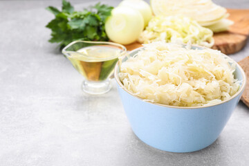 Bowl of tasty sauerkraut and ingredients on grey table, space for text