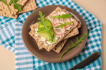 Tasty crispbreads with cream cheese, fresh cucumbers, radish and arugula served on beige table