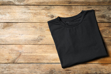 Stylish black T-shirt on wooden table, top view. Space for text