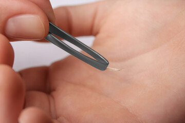 Woman pulling splinter from hand using tweezers on white background, closeup