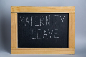 Small chalkboard with phrase Maternity Leave on grey background