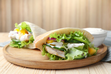 Delicious pita sandwiches with chicken breast and vegetables on wooden table, closeup