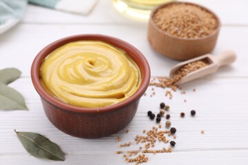 Bowl with delicious mustard and seeds on white wooden table, closeup. Space for text