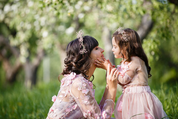 Mother and little daughter hugging in blooming apple garden. Mom loves her child. Spring story. Family look romantic similar dresses. Happy family in beautiful spring day