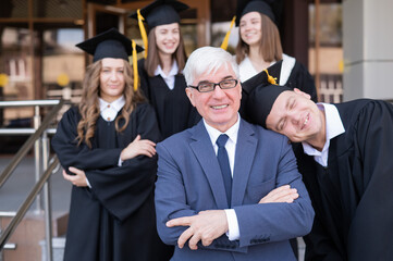 A gray-haired male teacher congratulates students on their graduation from the university. 