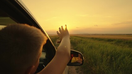 Happy teenager guy rides in a car, waving his hand out the car window. Road travel concept. The boy...