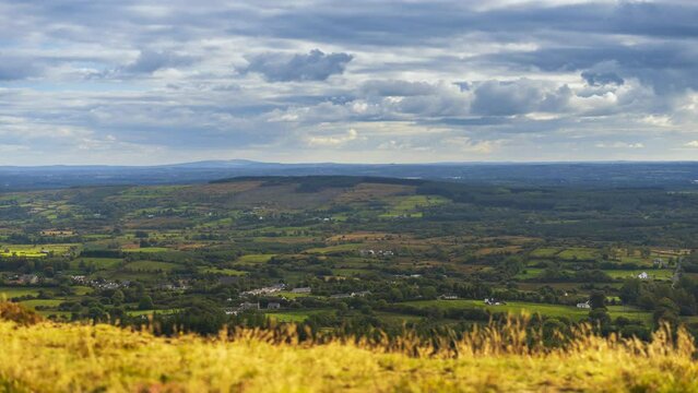 Time lapse of blurry grass in foreground and rural landscape in distance during a cloudy sunny day viewed from above Lough Meelagh in county Roscommon in Ireland.