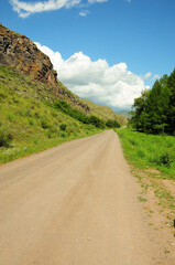 Straight gravel road running through the forest along a high cliff on a summer sunny day.