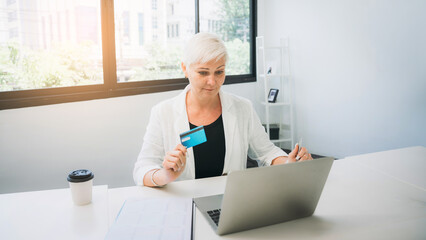 Woman holding a credit card and using a laptop computer to work online, shop online and do banking online.