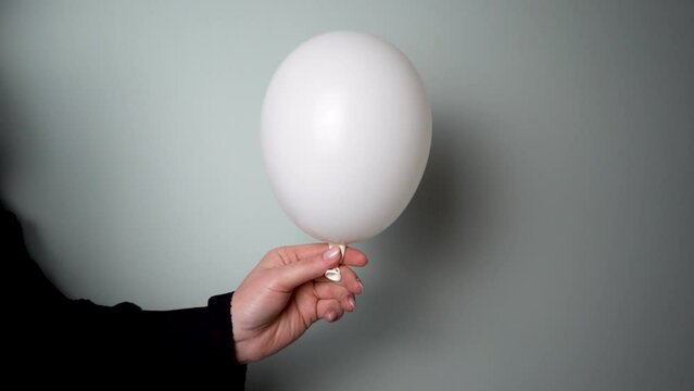 Young Woman Popping a White Balloon Against Grey Background