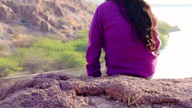 isolated young girl at mountain top with lake view backbit shot from flat angle video is taken at kaylana lake jodhpur rajasthan india.