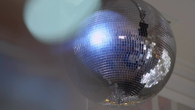Silver mirror disco ball suspended from the ceiling rotates quickly, light spot rays and glare. White stage light at a concert hall, club, party or disco. Illumination and atmosphere.
