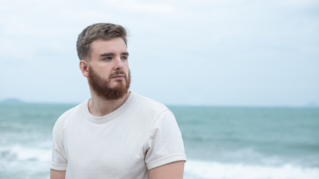 Portrait of young handsome bearded pensive man with beard is enjoy walk on summer beach near sea, breathe deep fresh air in tropical country. Summer vacation.
