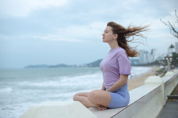 Fototapeta na wymiar Young calm sad serious woman is sitting on embankment near sea, ocean on beach, girl thinking, meditate on natural background 